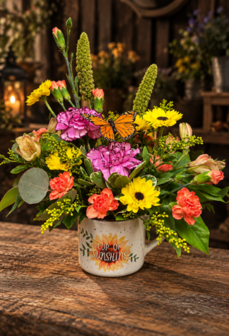 Cup of Sunshine colorful flower arrangement in a sunflower keepsake mug with yellow blooms, pink and coral carnations, garden greenery and a butterfly accent.