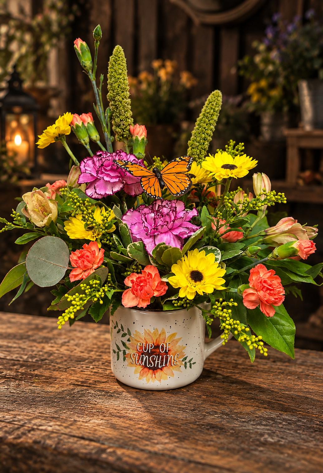 Cup of Sunshine colorful flower arrangement in a sunflower keepsake mug with yellow blooms, pink and coral carnations, garden greenery and a butterfly accent.